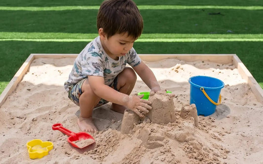 Niño jugando tranquilo con arena limpia Cimic en un arenero de madera, sin polvo