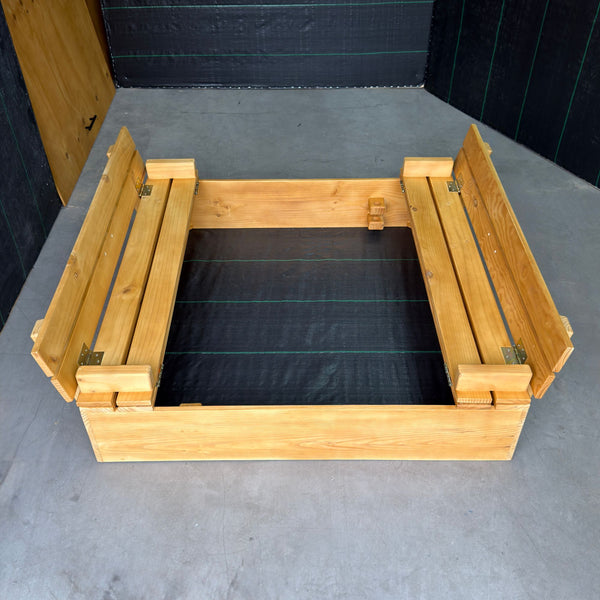 Arenero de madera para niños de 120 × 120 cm con la tapa abierta en dos bancas con respaldo, malla antimaleza en el fondo
