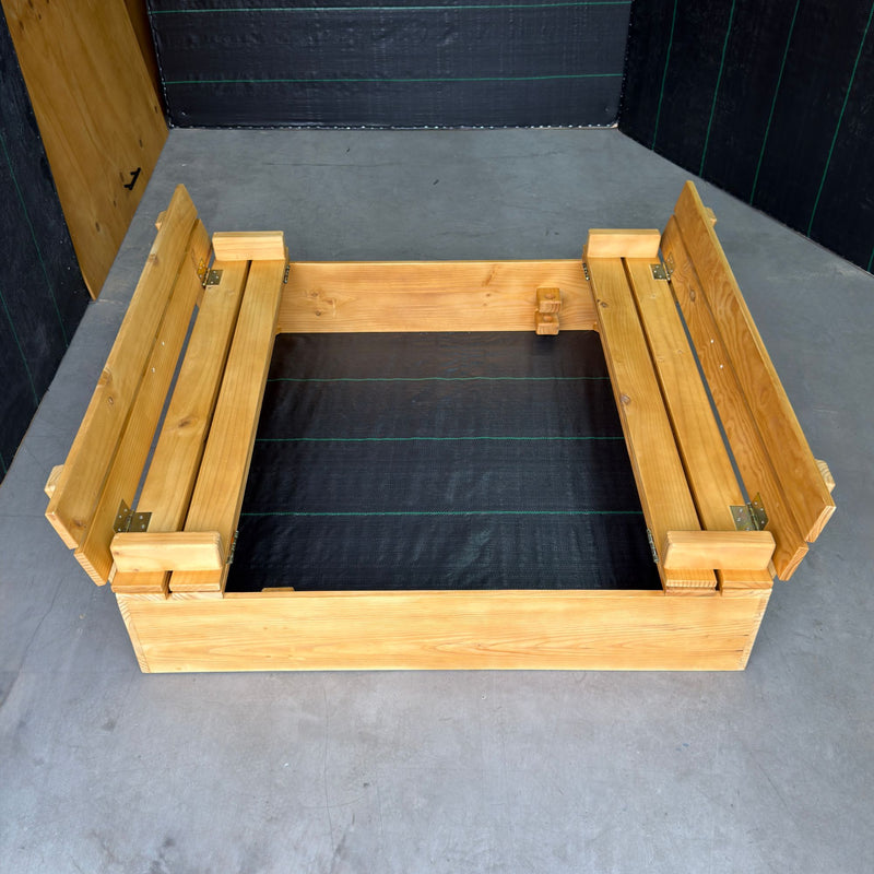 Arenero de madera para niños de 120 × 120 cm con la tapa abierta en dos bancas con respaldo, malla antimaleza en el fondo