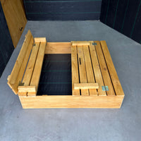 Arenero de madera para niños de 120 × 120 cm con una mitad de la tapa cerrada y la otra abierta como banca