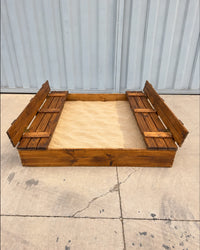 Arenero de madera para niños de 150 × 150 cm visto de frente, con arena y las dos bancas abiertas