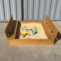 Arenero de madera para niños de 150 × 150 cm abierto, con las dos tapas convertidas en bancas