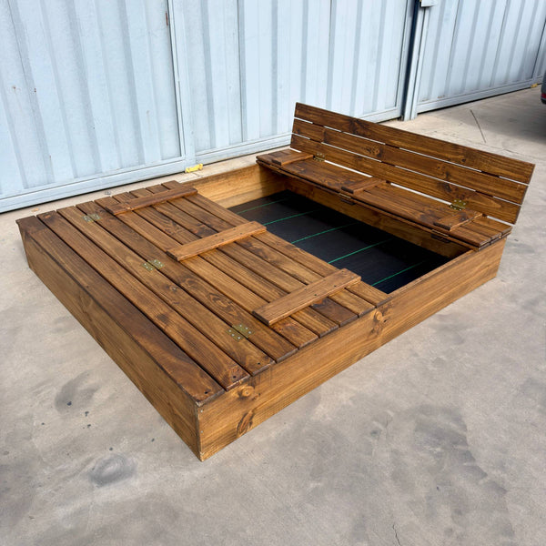 Arenero de madera para niños de 180 × 150 cm con una tapa cerrada y la otra abierta como banca con respaldo, malla antimaleza en el fondo