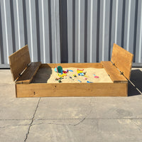 Arenero infantil de madera de 180 × 150 cm visto de frente, con arena Cimic y juguetes