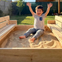 Niño feliz dentro del arenero de madera Cimic con las bancas plegables abiertas